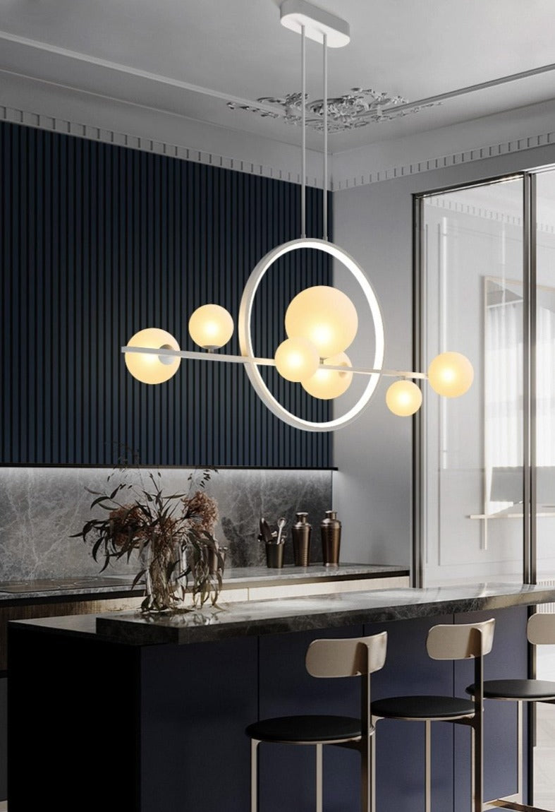 Modern pendant light with glass globes and a circular LED ring above a stone kitchen island in white.